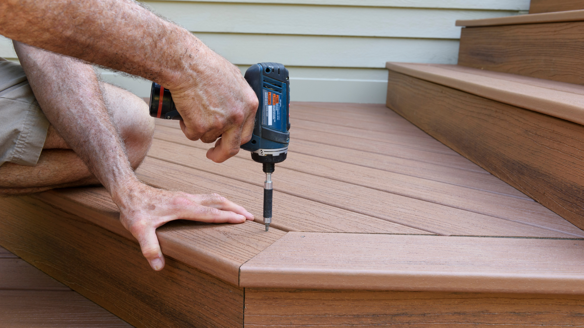 A craftsman drilling into wooden decking using an electric drill